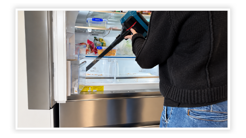 Vacuum with a long hose attachment cleaning onion skins and seeds out of a fridge crisper drawer